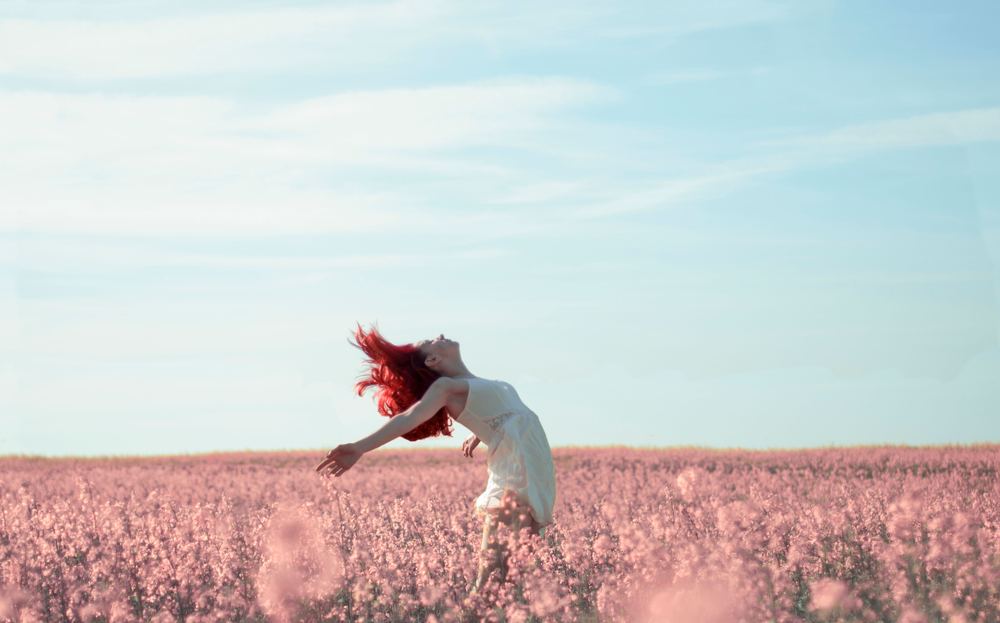 Mujer estirándose con libertad en un campo de flores rosas