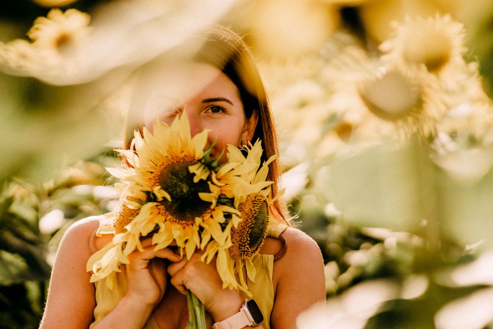 Mujer sosteniendo girasoles ante su rostro en un campo iluminado